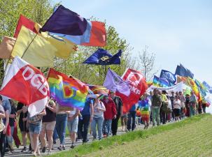 Demozug zum Ostermarsch - Eine Gruppe von Menschen geht auf einem Weg und tr&auml;gt verschiedene Flaggen, darunter Regenbogen- und politische Fahnen. - FrieKoop | flickr - CC BY-NC 2.0