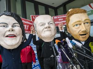 Eine Demo mit Masken der Gesichter von Scholz, Baerbock und Lindner