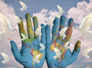 Zwei offene Handflächen sind mit einer Weltkarte bemalt, im Hintergrund fliegen weiße Tauben vor einem blauen Wolkenhimmel in der Luft.