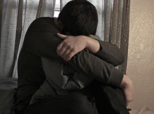 Ein Mensch sitzt auf dem Bett und sieht deprimiert aus