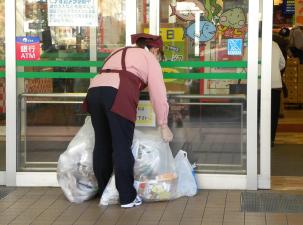 Eine Frau verr&auml;umt M&uuml;lls&auml;cke vor einem Ladengesch&auml;ft