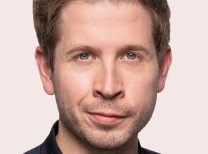 Foto von Kevin K&uuml;hnert: Ein Mann mit kurzen, blonden Haaren und einem neutralen Gesichtsausdruck. Er tr&auml;gt ein dunkelblaues Oberteil. Hintergrund ist hell.