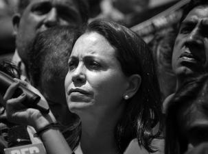 Black and white image of Venezuelan politician María Corina Machado. She looks seriously off to one side standing in a crowd of people.