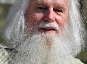 Porträt von Matthias Reichl in 2021 - Ein älterer Mann mit langem, grauem Bart und weißen Haaren, lächelt freundlich in einer natürlichen, sonnigen Umgebung.