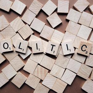 Beigefarbene hölzerne Scrabble-Buchstaben buchstabieren das Wort Politik auf vielen anderen leeren quadratischen Stücken