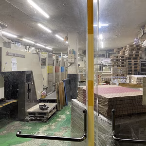 Ein Blick in eine Produktionshalle mit Maschinen, Regalen und Materialien auf dem Boden. Die Beleuchtung ist hell und die Umgebung wirkt industriell.