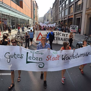 Demonstration auf der Stra&szlig;e mit mehreren Menschen, die Banner mit Forderungen halten. Sonniger Tag, urbanes Umfeld.