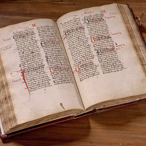 Ein aufgeschlagenes, altert&uuml;mliches Buch mit handgeschriebenem Text und roter Tinte, auf einem Holztisch.