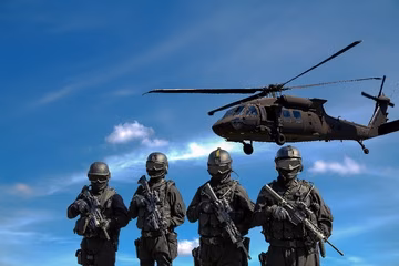 Vier Soldaten des Milit&auml;rs stehen bewaffnet unter einem fliegenden Hubschrauber.