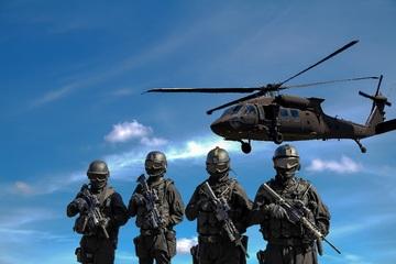 Vier Soldaten des Militärs stehen bewaffnet unter einem fliegenden Hubschrauber.