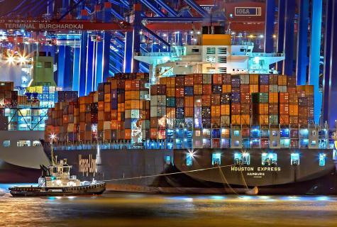Riesiges Containerschiff, das nachts mit Tausenden von Schiffscontainern mit leuchtenden Lichtern in einen Hafen einfährt