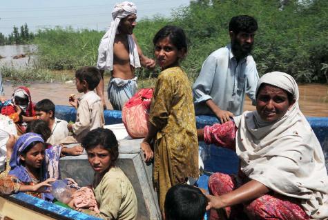 Viele pakistanische Kinder und eine Frau sitzen in einem mit Habseligkeiten gefüllten Boot auf dem schmutzigen Hochwasser, während zwei Männer das Boot von außen steuern