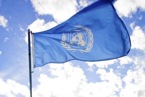 Hellblaue Flagge, die im Wind weht, mit dem weißen UN-Logo in der Mitte | Blauer Himmel und weiße Wolken im Hintergrund