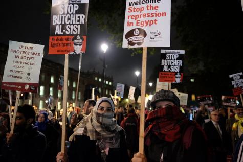 Viele Menschen stehen in der kalten Nacht und protestieren mit Transparenten und Plakaten gegen die Unterdr&uuml;ckung in &Auml;gypten. Im Vordergrund sind zwei Frauen zu sehen, die ihre Gesichter verbergen.