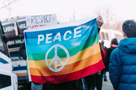 Eine Flagge mit Regenbogenfarben und einem Peace zeichen darauf, bei einer Demonstration für den Frieden in Salzburg.  In Salzburg kann man sich freiwillig für den Frieden engagieren.