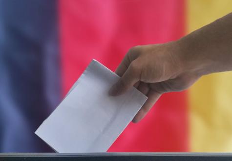 Eine Hand wirft einen Wahlumschlag in eine Wahlurne