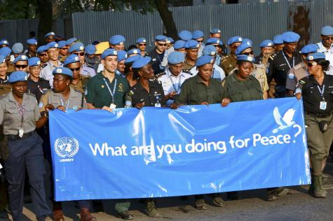 Friedenssoldaten der Vereinten Nationen halten in ihren Uniformen und blauen Hüten bekleidet, ein riesiges blaues Transparent mit der Aufschrift "Was macht ihr für den Frieden?