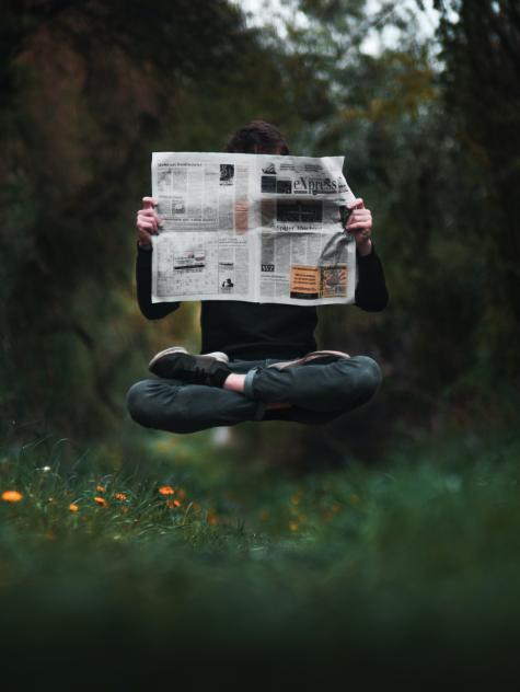 EIne Mann liest schwebend eine Zeitung im Wald