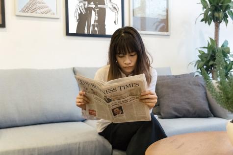 Eine Frau liest eine Tageszeitung auf einer Couch