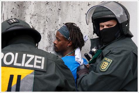 Zwei Polizisten nehmen eine Person mit Migrationshintergrund fest