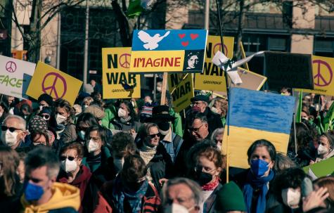 Viele Anti-Kriegs-Demonstranten stehen auf der Stra&szlig;e und halten Plakate mit der blau-gelben Flagge der Ukraine und der Aufschrift "No War" in die H&ouml;he.