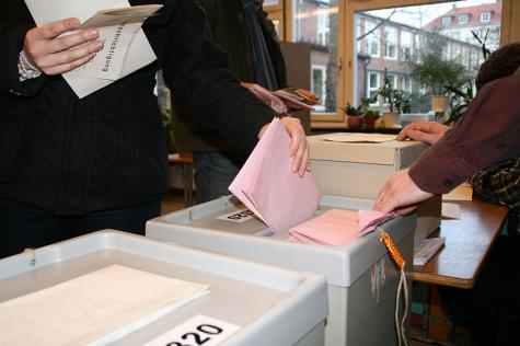 Eine Person schmeißt ihre Wahlunterlagen in die Wahlurne