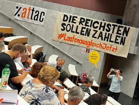Eine Vorlesung vor einem Attac-Banner f&uuml;r mehr Reichensteuern