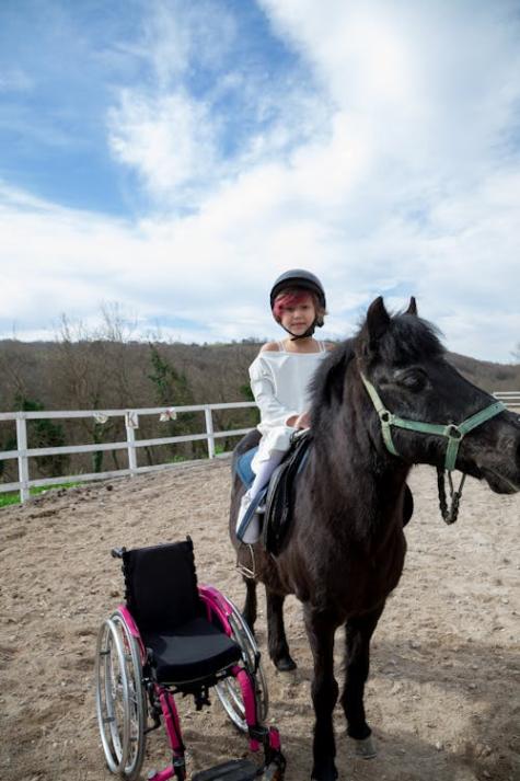 Gel&auml;hmtes Kind auf einem Pferd mit Rollstuhl daneben