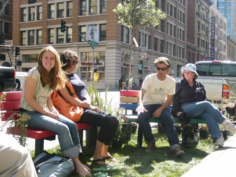 Vier Menschen sitzen auf B&auml;nken auf einem Parkplatz