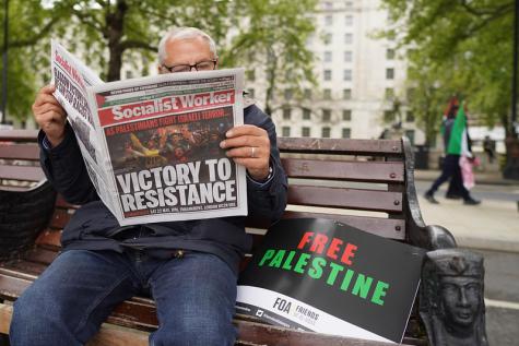 Ein Mann liest eine Zeitung neben einem Pro-Gaza Schild