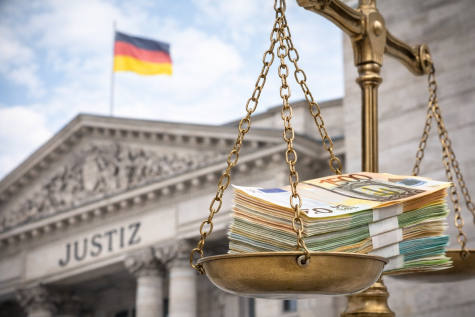Eine goldene Waage mit Geldscheinen im Vordergrund, im Hintergrund das Justizgeb&auml;ude mit der deutschen Flagge.
