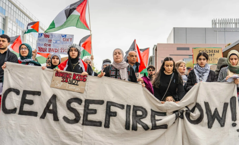 Protestierende stehen auf der Stra&szlig;e und fordern ein Ende der K&auml;mpfe in Gaza. Sie halten ein gro&szlig;es wei&szlig;es Banner mit der Aufschrift &bdquo;Ceasefire Now&ldquo;
