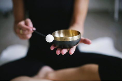Eine Person sitzt im Schneidersitz und hält eine Schale mit goldenem Rand und einem kleinen Schlägel in der Hand.