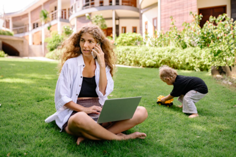 Mutter mit Laptop im Garten, Kind spielt daneben