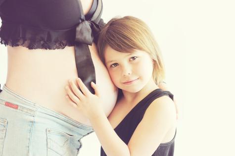 Geschwisterkind kuschelt an Babybauch