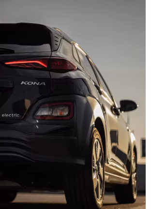 Der Blick auf das Heck eines schwarzen Hyundai Kona Elektro unter einem klaren Himmel, mit gl&auml;nzenden Felgen und zur&uuml;ckhaltendem Licht.