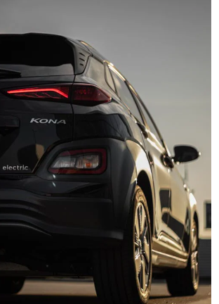 Der Blick auf das Heck eines schwarzen Hyundai Kona Elektro unter einem klaren Himmel, mit gl&auml;nzenden Felgen und zur&uuml;ckhaltendem Licht.