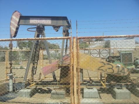 Eine alte &Ouml;lbohranlage, eingez&auml;unt, bei klarem Himmel. Rostige Teile und staubige Umgebung sind sichtbar.