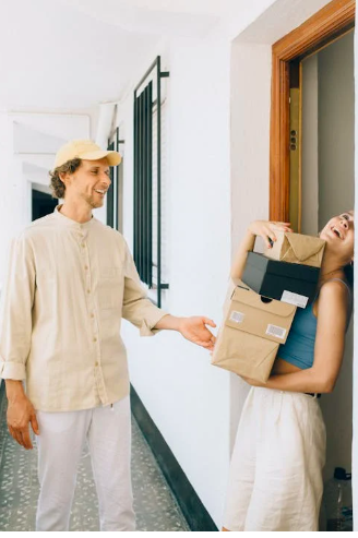 Lieferant &uuml;bergibt Pakete an l&auml;chelnde Frau, die an einer Wohnungst&uuml;r steht. Heller und freundlicher Innenraum.