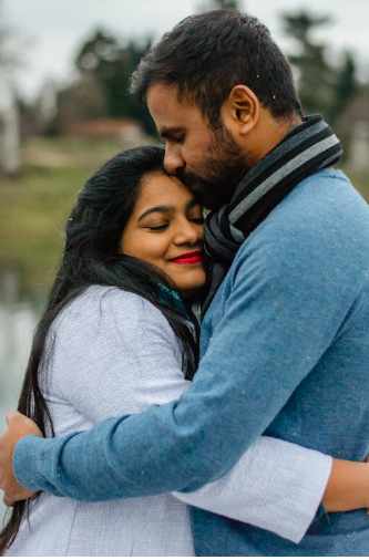 Ein Paar umarmt sich liebevoll am Wasser, umgeben von einer nat&uuml;rlichen Umgebung. Die Frau l&auml;chelt, w&auml;hrend der Mann sie z&auml;rtlich k&uuml;sst.