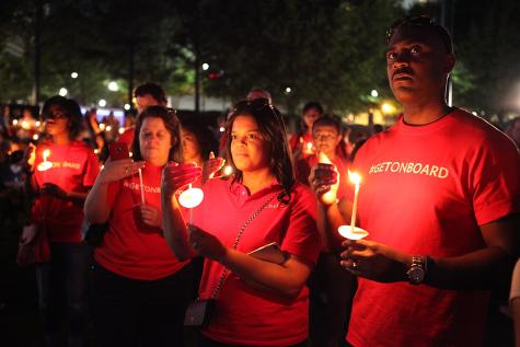 Eine Gruppe von Menschen in roten T-Shirts h&auml;lt Kerzen in der Dunkelheit, sichtbar ernst und nachdenklich.