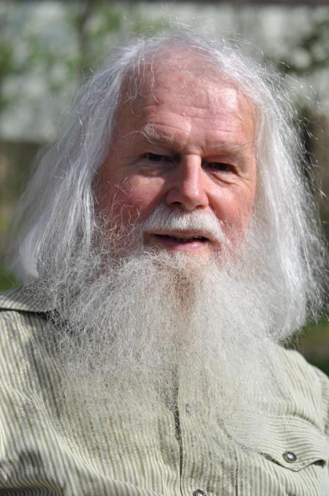 Portr&auml;t von Matthias Reichl in 2021 - Ein &auml;lterer Mann mit langem, grauem Bart und wei&szlig;en Haaren, l&auml;chelt freundlich in einer nat&uuml;rlichen, sonnigen Umgebung.