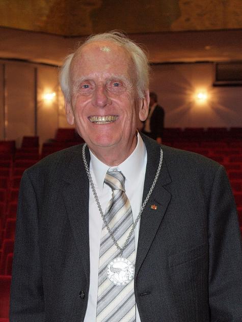 Ulrich Gottstein anl&auml;sslich der Verleihung der Paracelsus-Medaille beim 114. Deutschen &Auml;rztetag in Kiel - Ein &auml;lterer Mann mit wei&szlig;em Haar, l&auml;chelt in einem Anzug mit Krawatte und einer Medaille, vor einem Theater mit roten Sitzreihen.