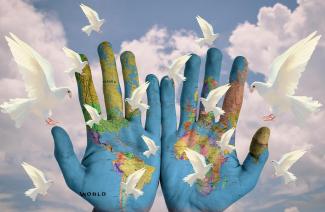 Zwei offene Handflächen sind mit einer Weltkarte bemalt, im Hintergrund fliegen weiße Tauben vor einem blauen Wolkenhimmel in der Luft.