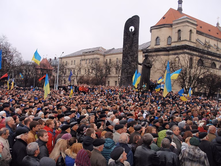 Regierungsfeindliche Demonstranten versammeln sich au&szlig;erhalb von Kiew. Unter grauem Himmel halten Tausende von Demonstranten blaue und gelbe Ukraine-Fahnen.